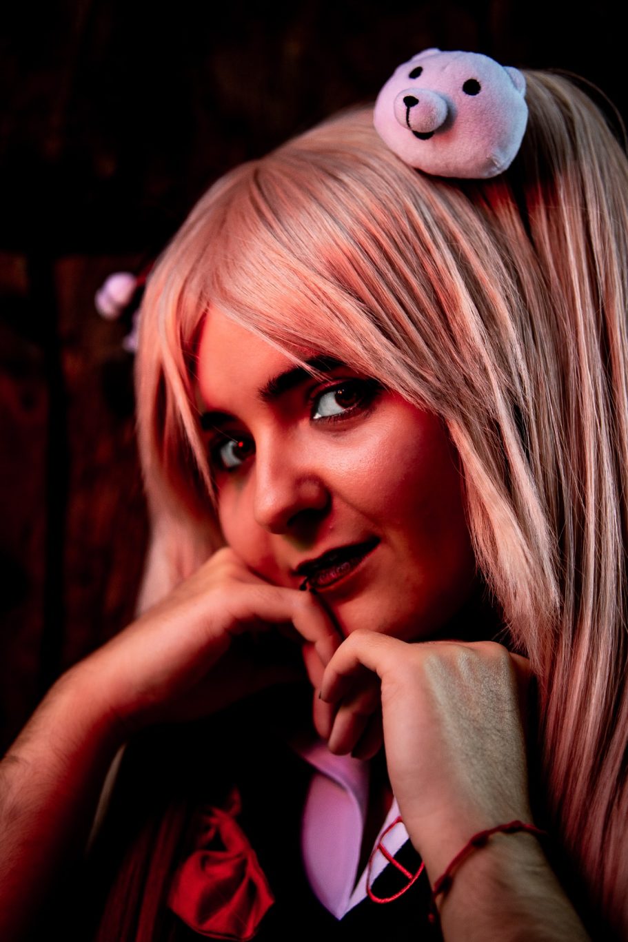 Chica con cabello largo y rubio, viste un disfraz y tiene un oso de peluche en la cabeza.