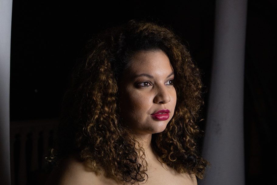 Retrato de una mujer con cabello rizado y labios rojos, iluminada suavemente.