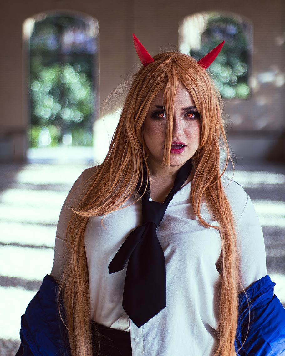 Mujer con cabello largo, cuernos rojos y camisa blanca, en un entorno luminoso.