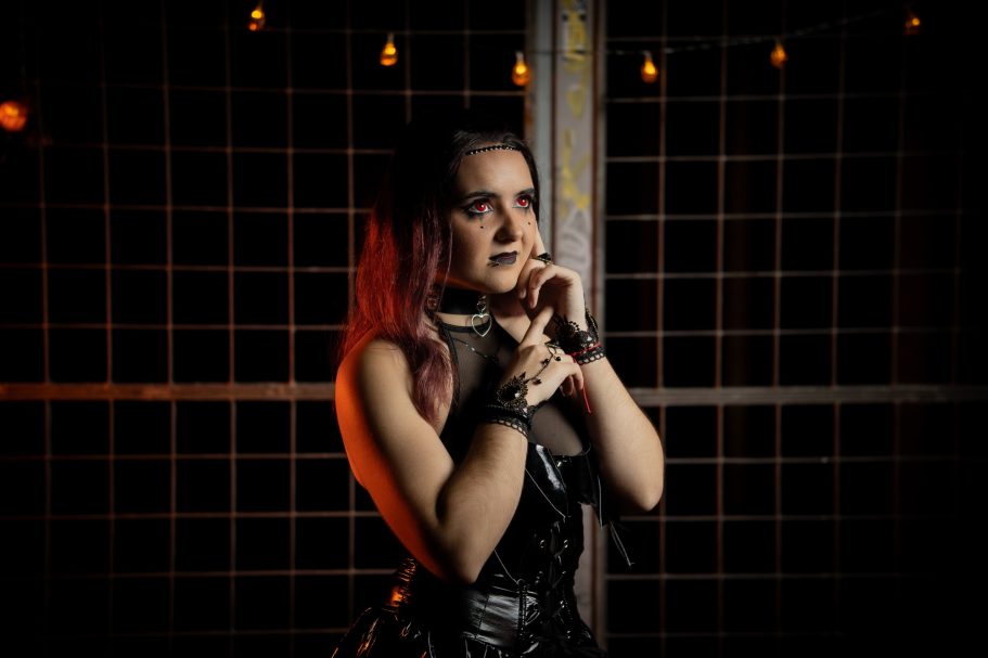 Mujer con cabello rojo y atuendo oscuro, posando en un fondo con luces tenue.