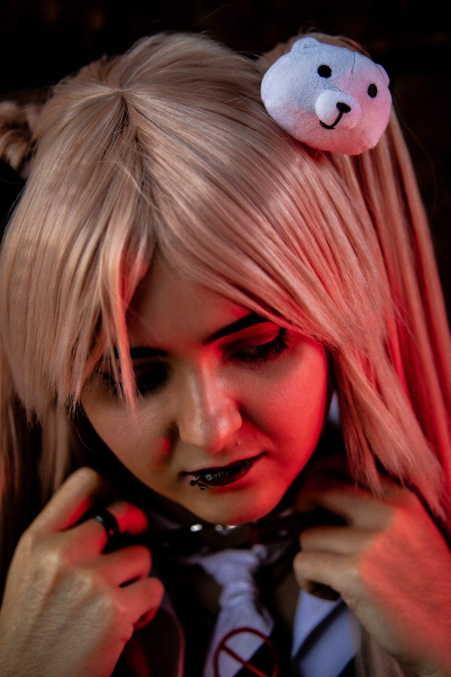 Joven con peluca rubia y diadema de oso, mirada seria en un ambiente con iluminación tenue.