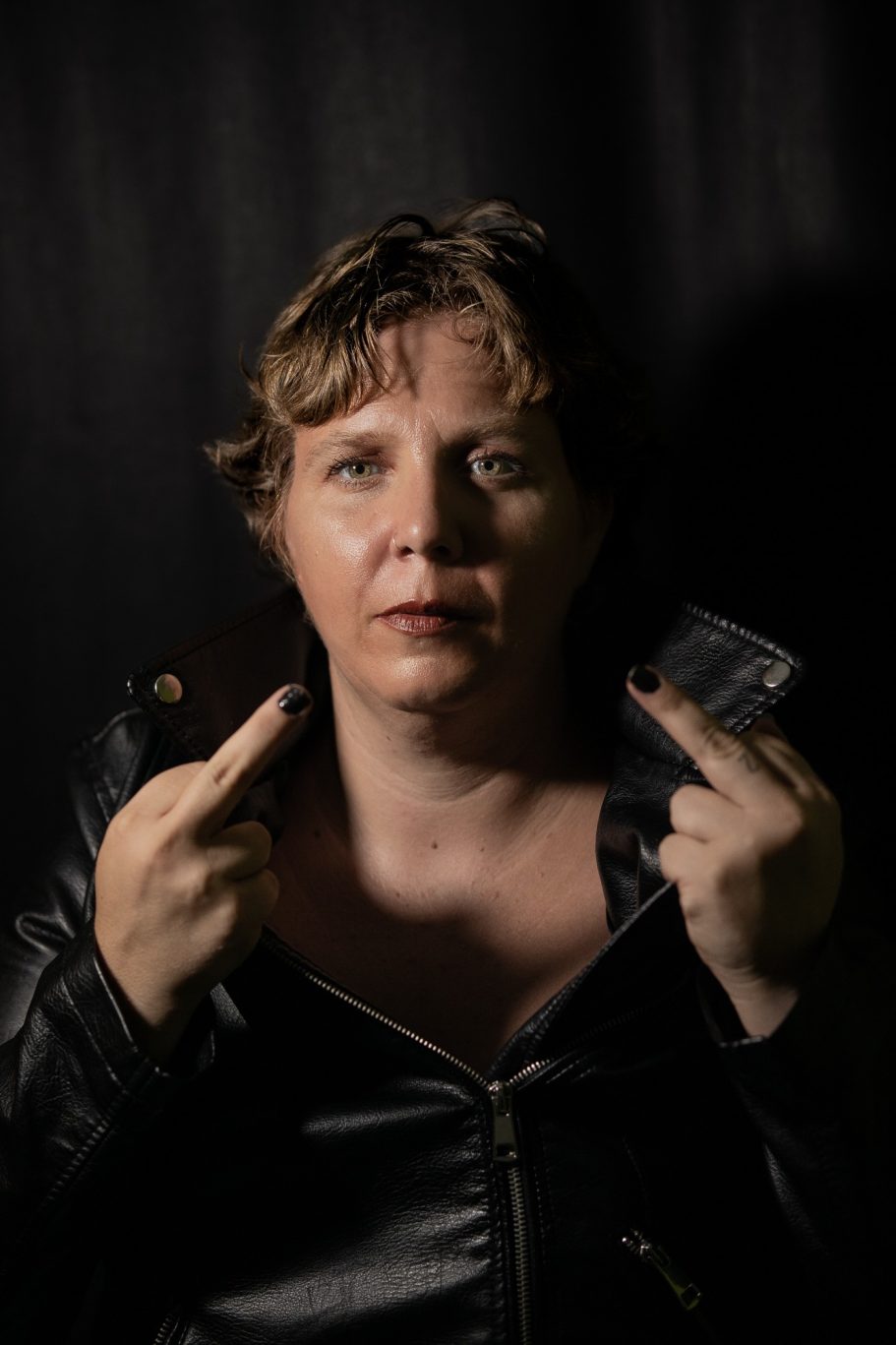 Mujer con cabello corto en un fondo oscuro, mostrando los dedos del medio.