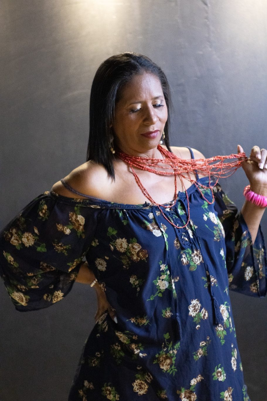 Mujer con blusa floral, sujetando collar rojo, con expresión introspectiva.