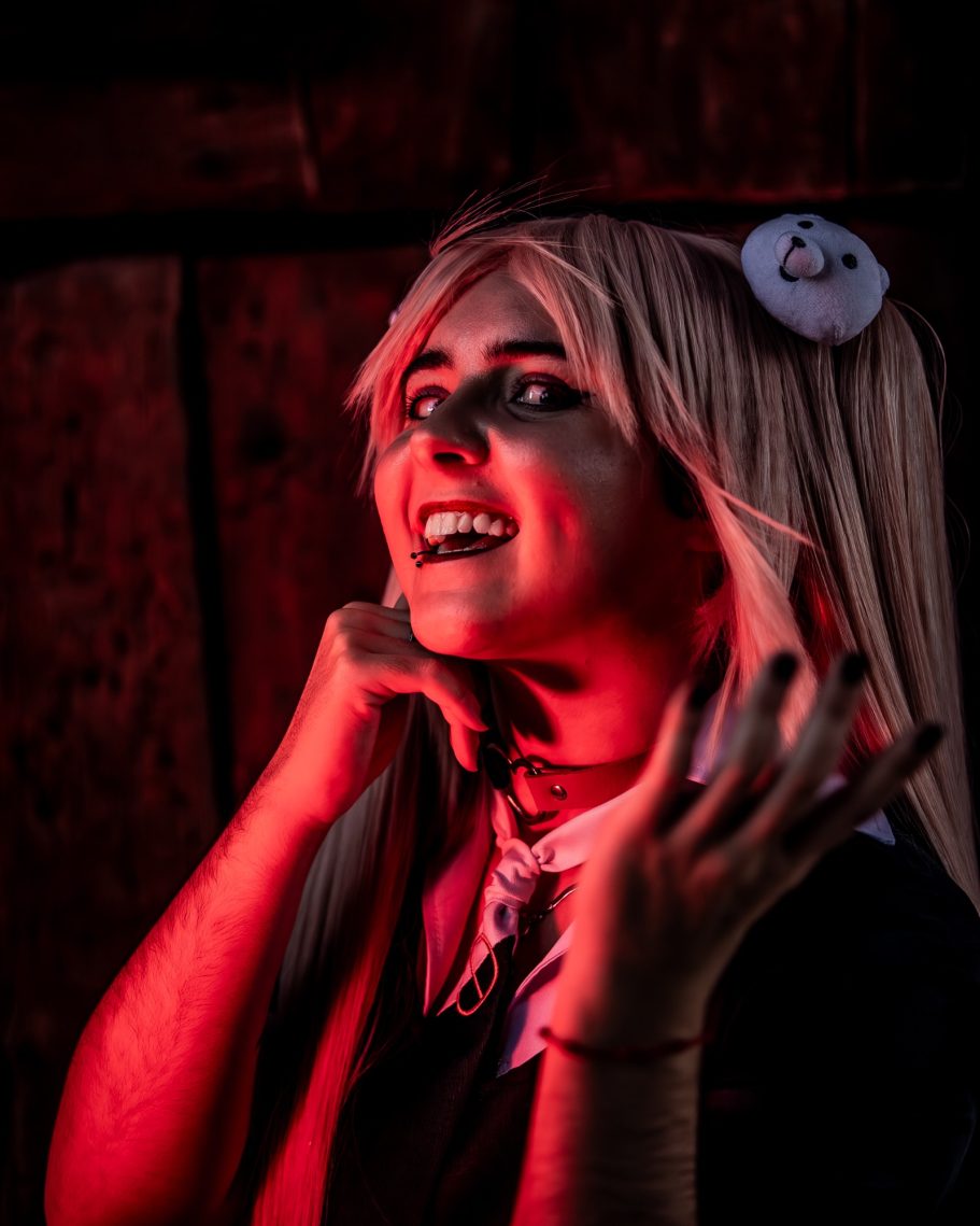 Persona con cabello largo y rubio, iluminada con luces rojas, en pose dramática.