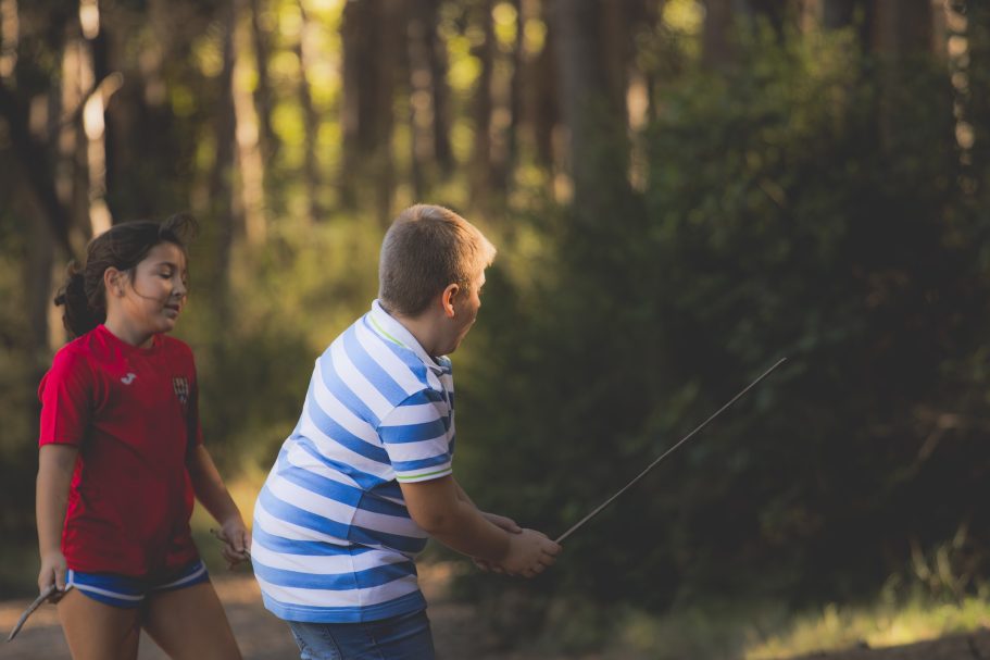 Niño lanzando una caña de pescar, niño sonriente observando en un entorno natural.