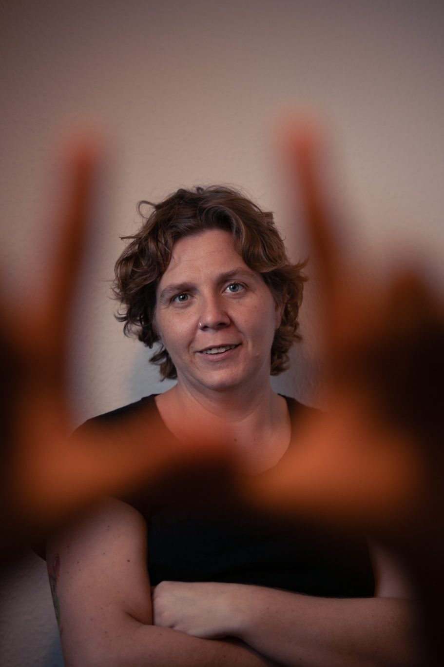 Mujer con cabello rizado, mirando a la cámara con gestos de manos en primer plano.
