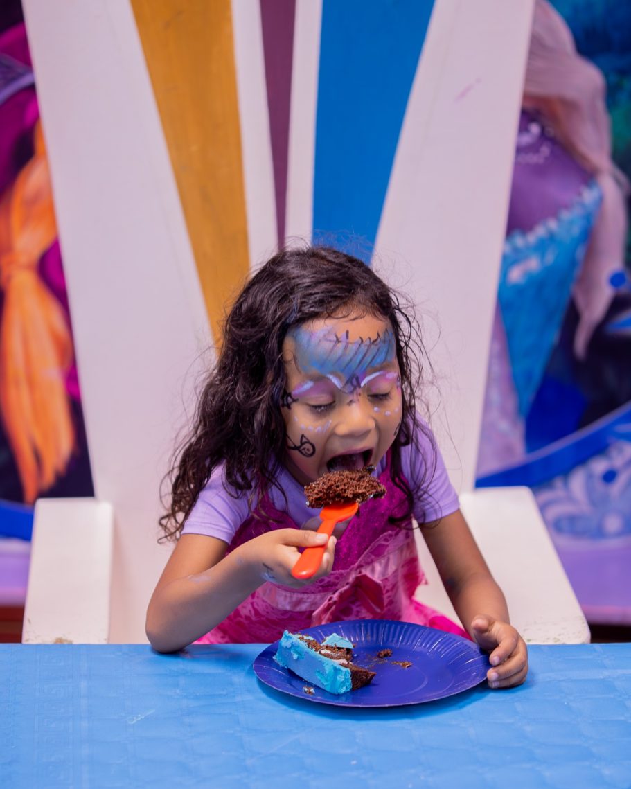 Niña comiendo un pastel de chocolate, con cara pintada y una expresión de alegría.