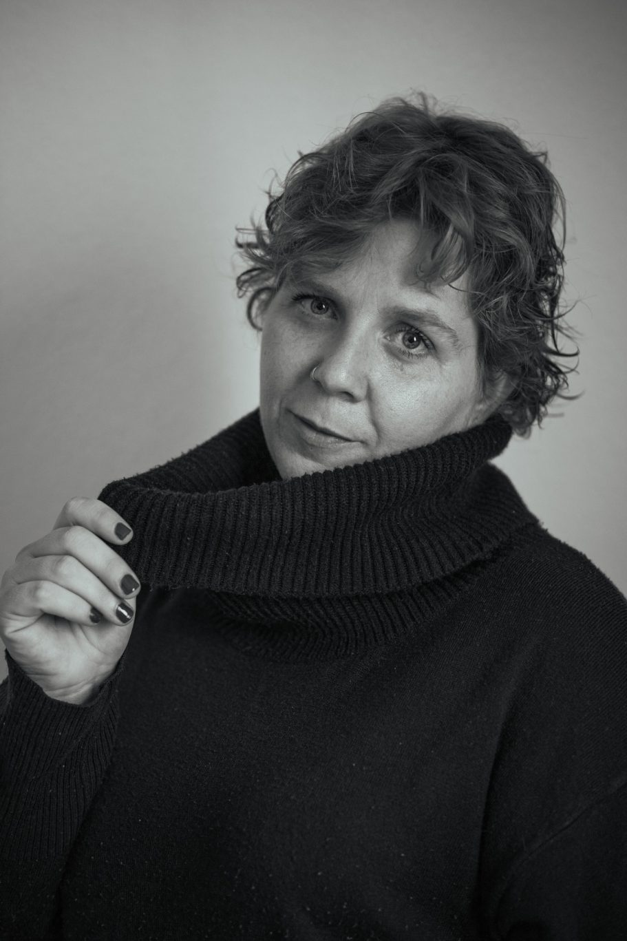 Mujer con cabello rizado, vistiendo un suéter negro, mirando a la cámara.