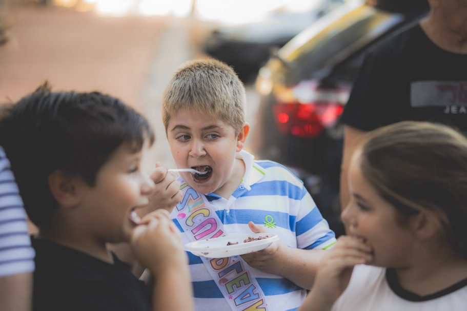Niños disfrutando de comida al aire libre, uno de ellos sorprendido al comer.