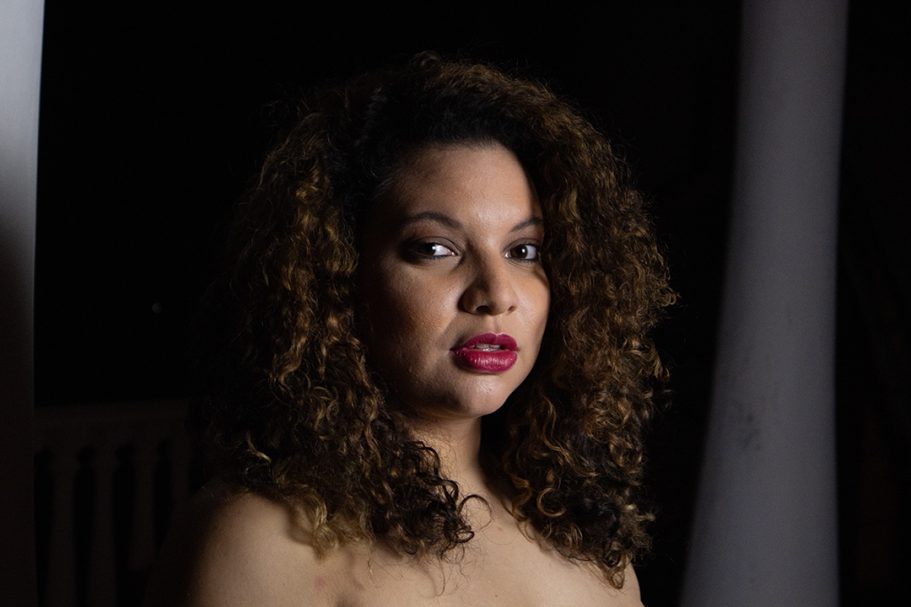 Mujer con cabello rizado y labios rojos, mirada seria en un entorno oscuro.