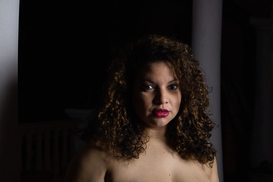 Mujer con cabello rizado y labios rojos, frente a un fondo oscuro.