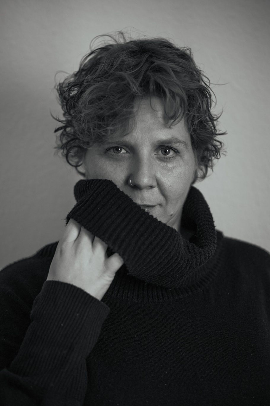 Mujer con suéter de cuello alto, mirando a la cámara con expresión contemplativa.