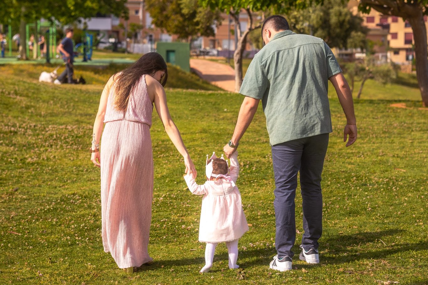 Una familia camina de la mano por un parque verde, con un niño pequeño al frente.