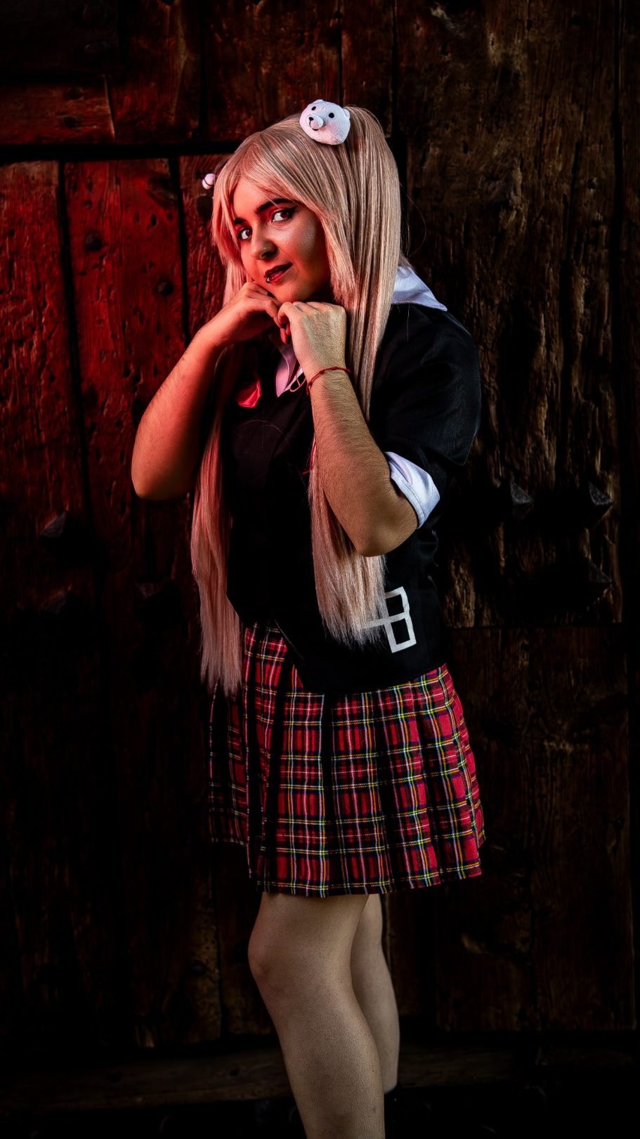 Chica con peluca larga, uniforme escolar y falda de cuadros, posando sonriente.