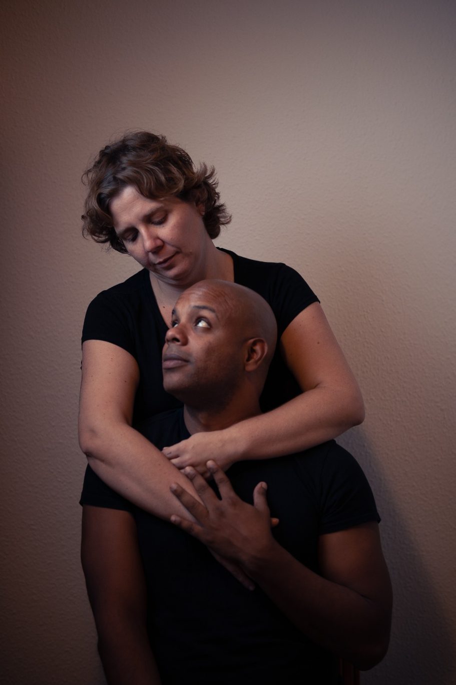 Mujer abrazando a un hombre, ambos mirando hacia arriba en un ambiente iluminado.