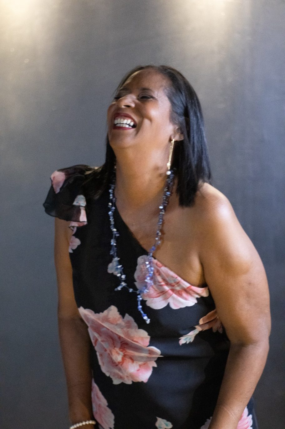 Mujer sonriente con un vestido negro con flores, riendo alegremente.