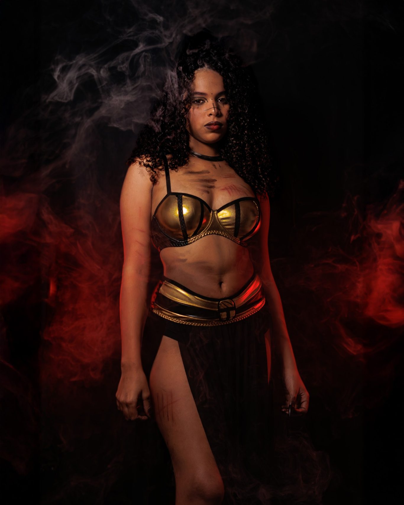 Mujer con armadura dorada, cabello rizado y fondo oscuro con humo.