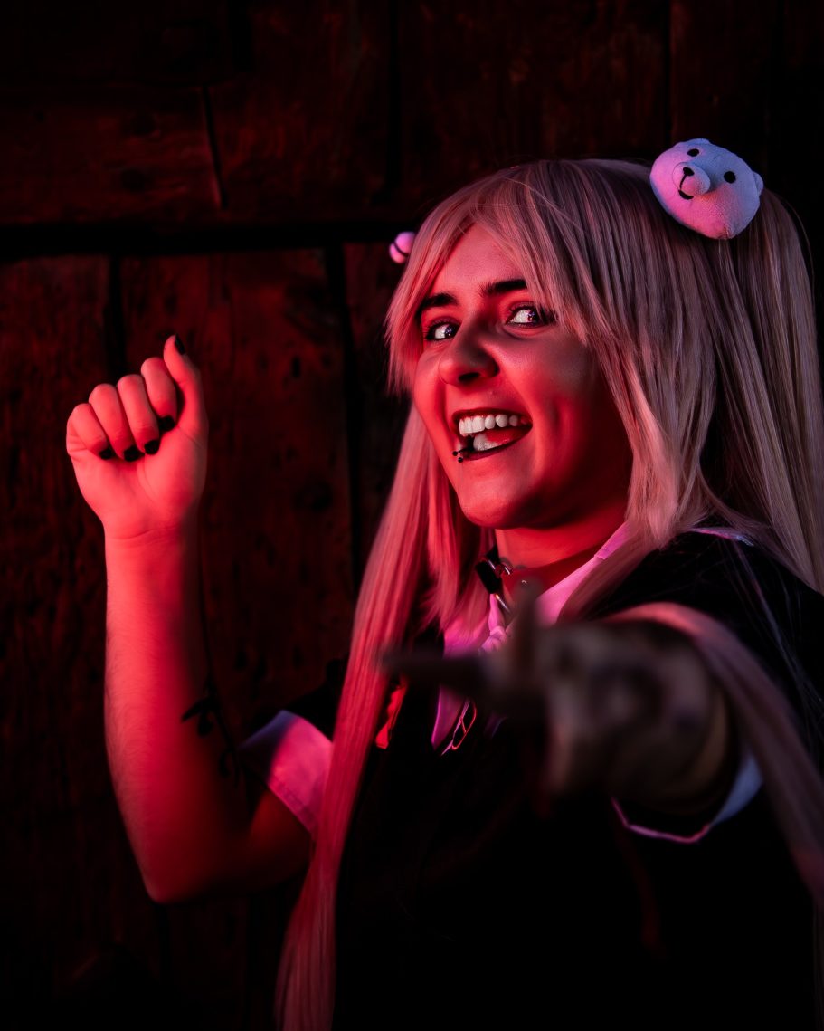 Joven con cabello largo y rubio, sonriendo mientras levanta el puño en un fondo oscuro.