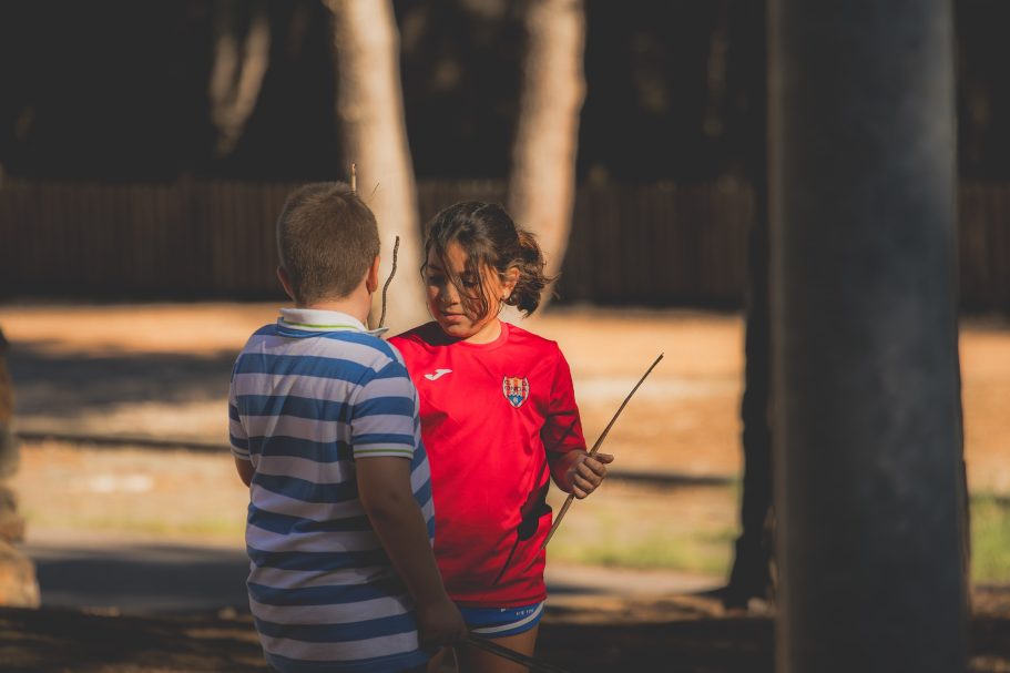 Niños conversando al aire libre, uno lleva una camiseta roja y el otro una de rayas.