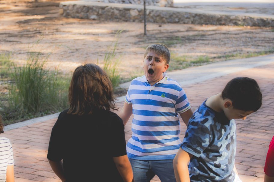 Niño con camiseta de rayas gritando mientras otros niños lo observan.