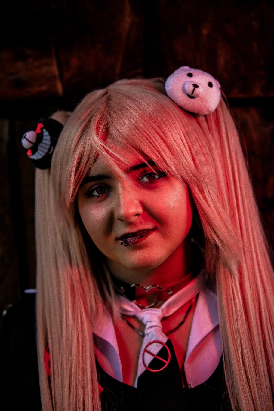 Chica con cabello largo y rubio, mirada intensa, vestimenta oscura y accesorios de peluche.