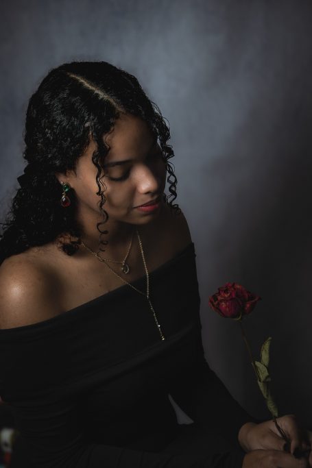Mujer con flores rojas, vestida en negro, mostrando una expresión reflexiva.
