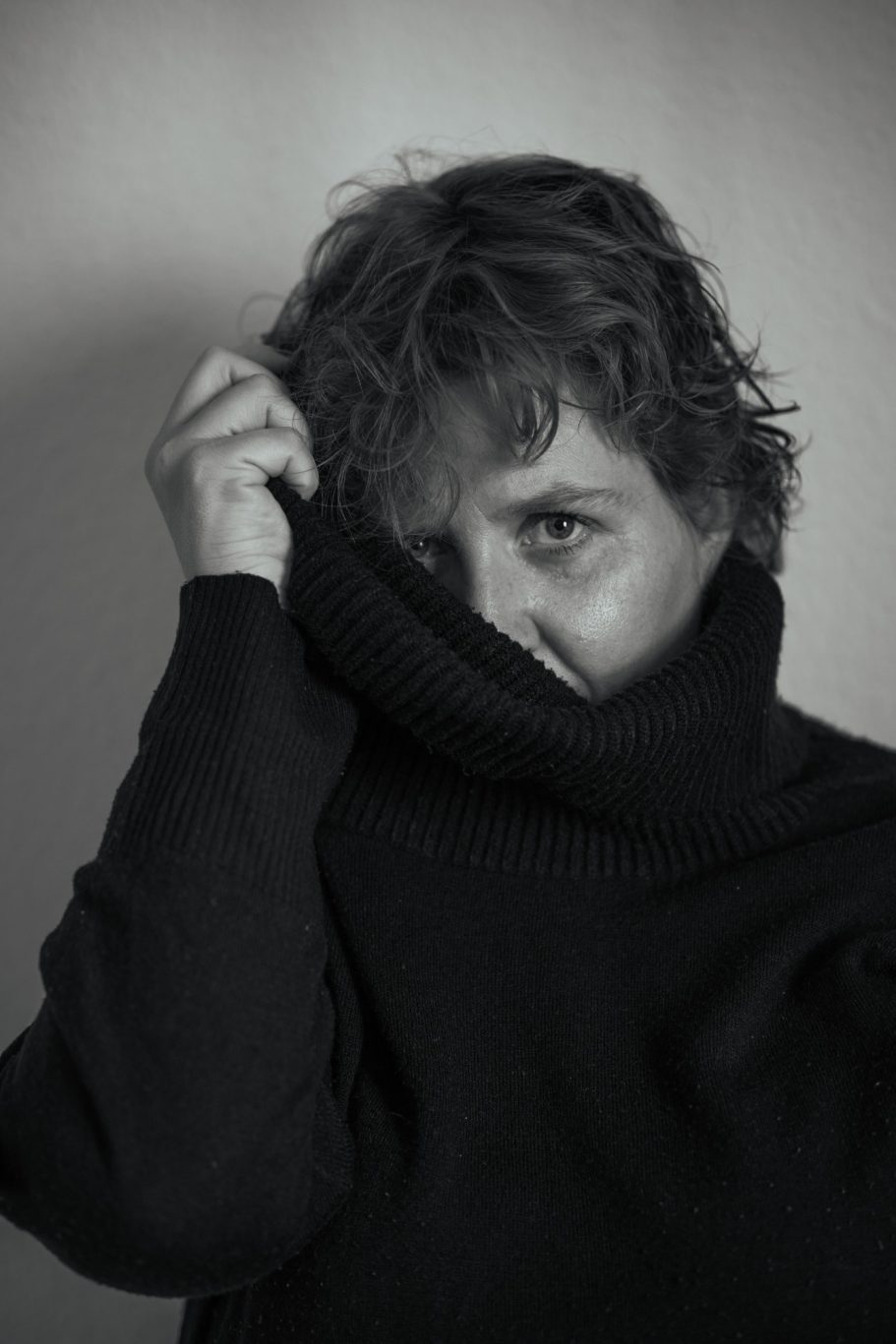 Persona con cabello desordenado, mirando con expresión pensativa, usa un suéter oscuro.