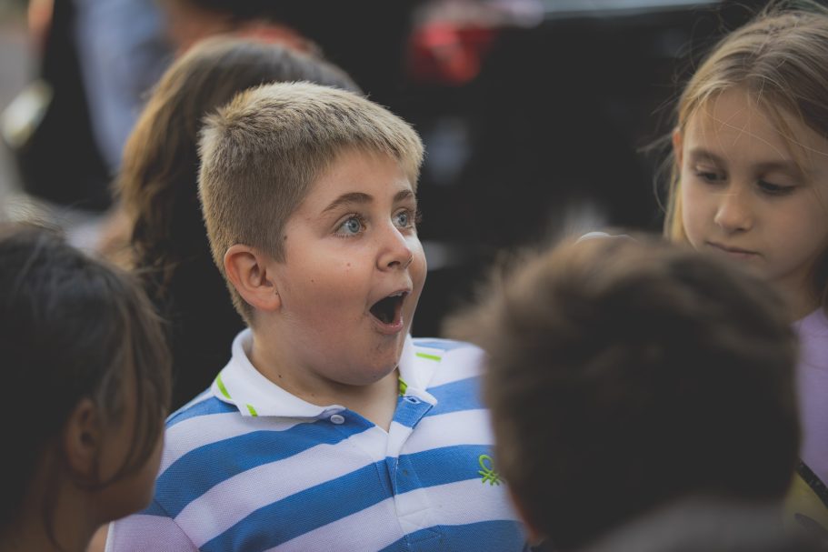 Niño sorprendido con camisa a rayas, rodeado de otros niños.