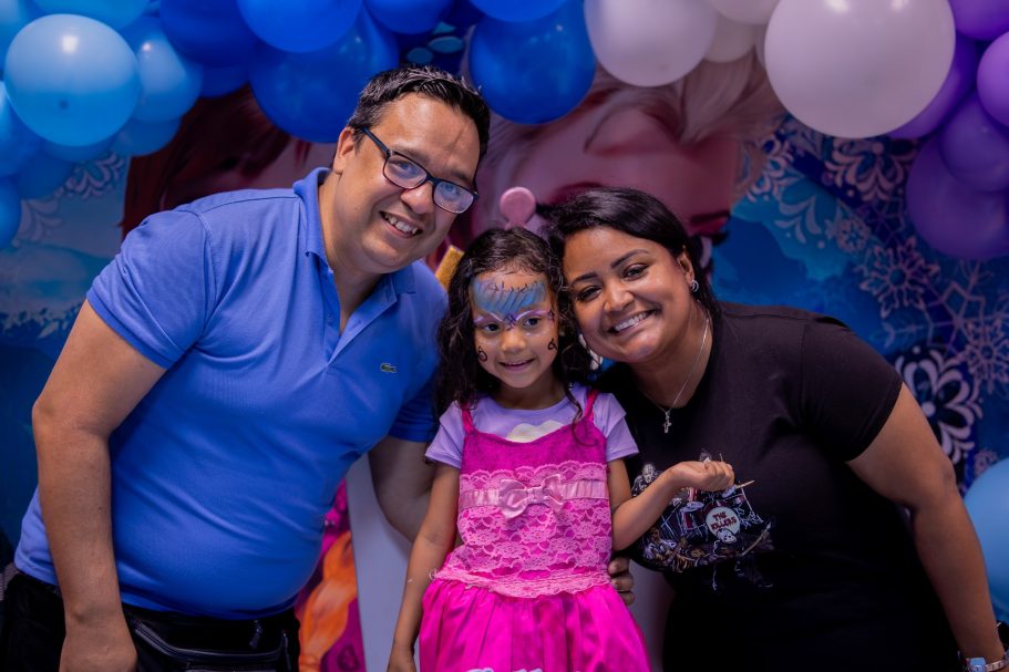Familia sonriente posando entre globos, con una niña en el centro y sus padres a los lados.
