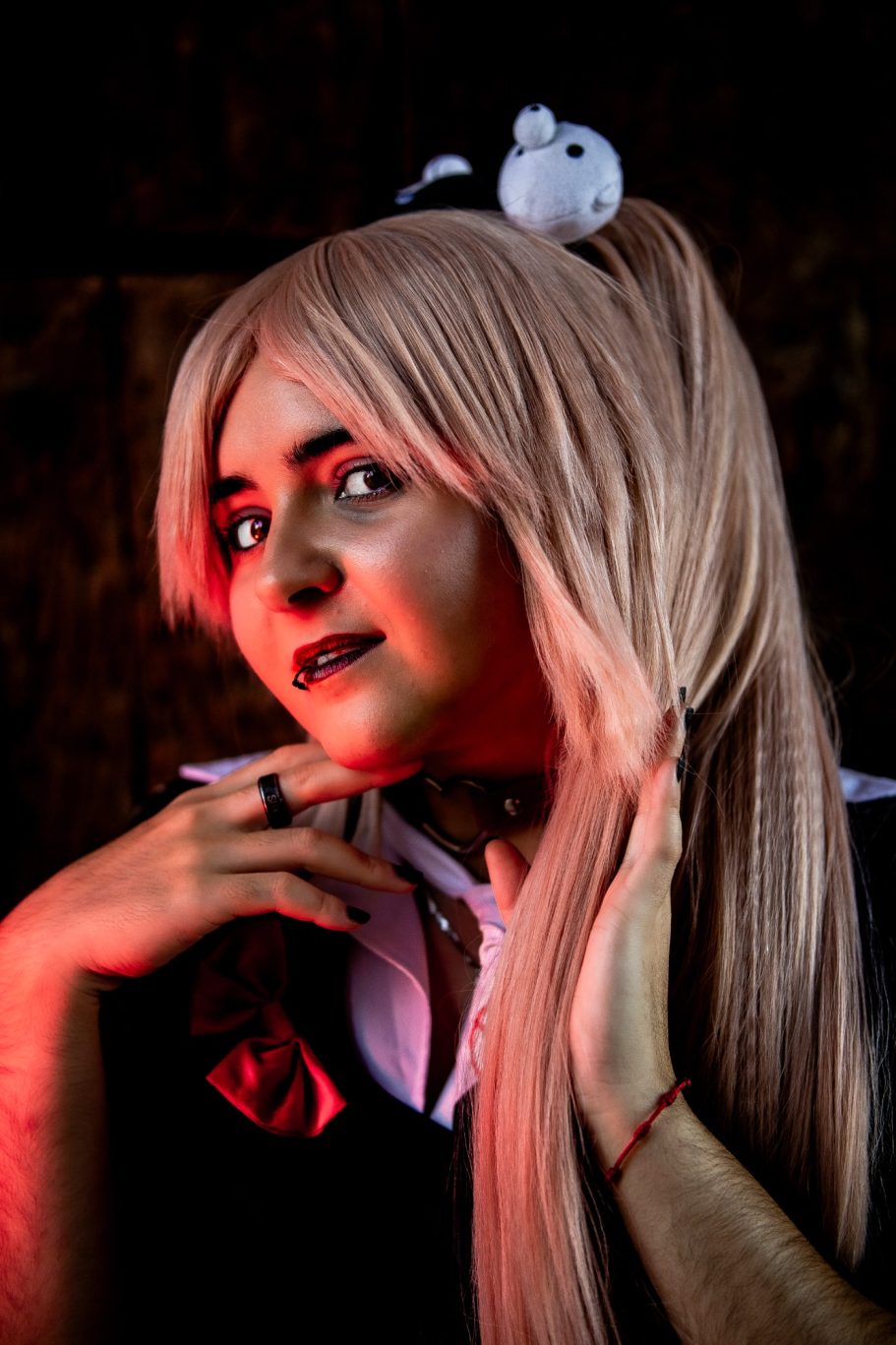 Cosplayer con cabello largo y rubio, vestida con un atuendo oscuro y detalles en blanco.