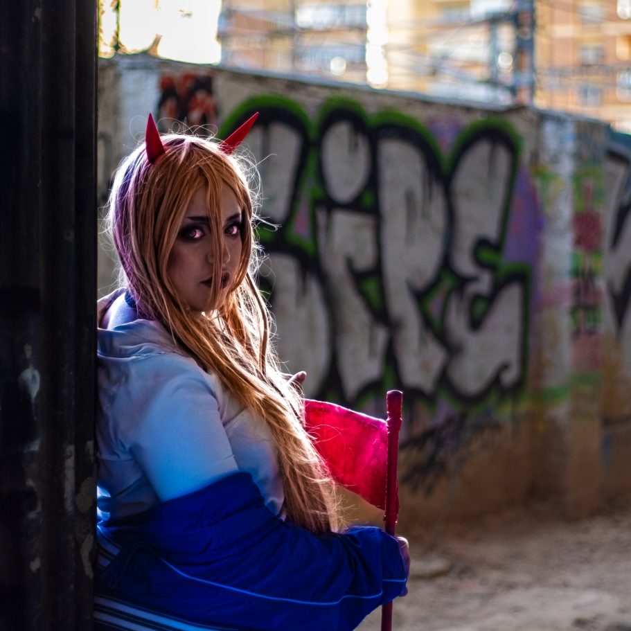Persona con cuernos rojos y cabello largo, sosteniendo una bandera en un fondo grafiteado.