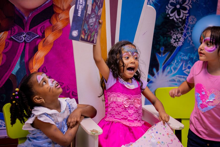 Niñas en una fiesta, una muestra emocionada un dibujo mientras las otras la observan.