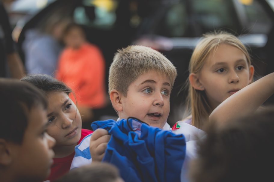 Niños observando atentamente a un chico que sostiene una prenda de ropa azul.