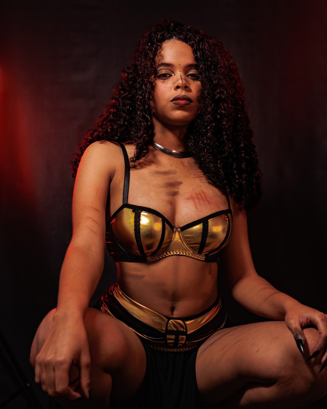 Mujer con cabello rizado, vestida con un top dorado y falda negra, posando con actitud fuerte.