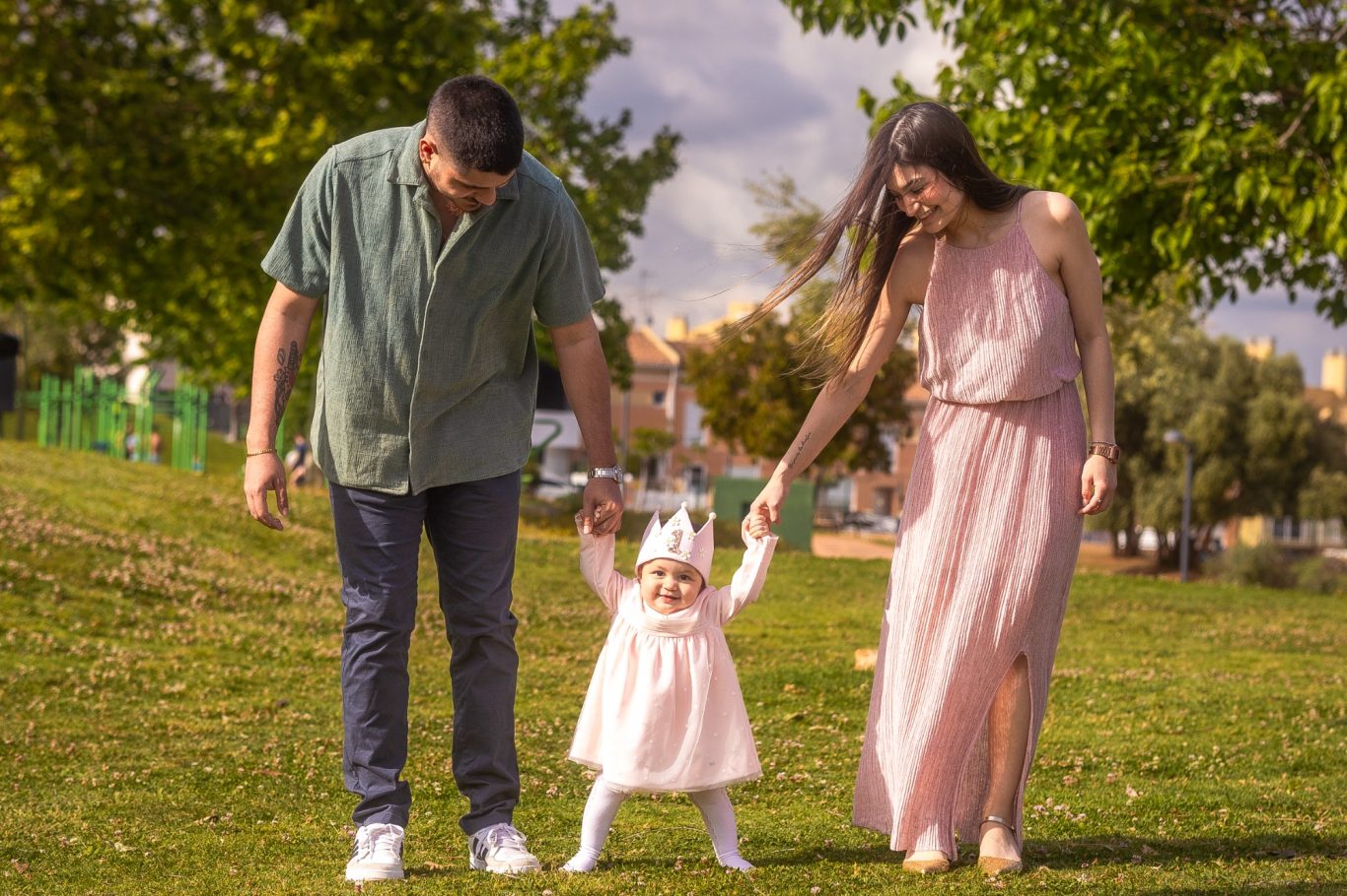 Familia de tres, dos adultos y una niña, caminando por un parque bajo un cielo nublado.