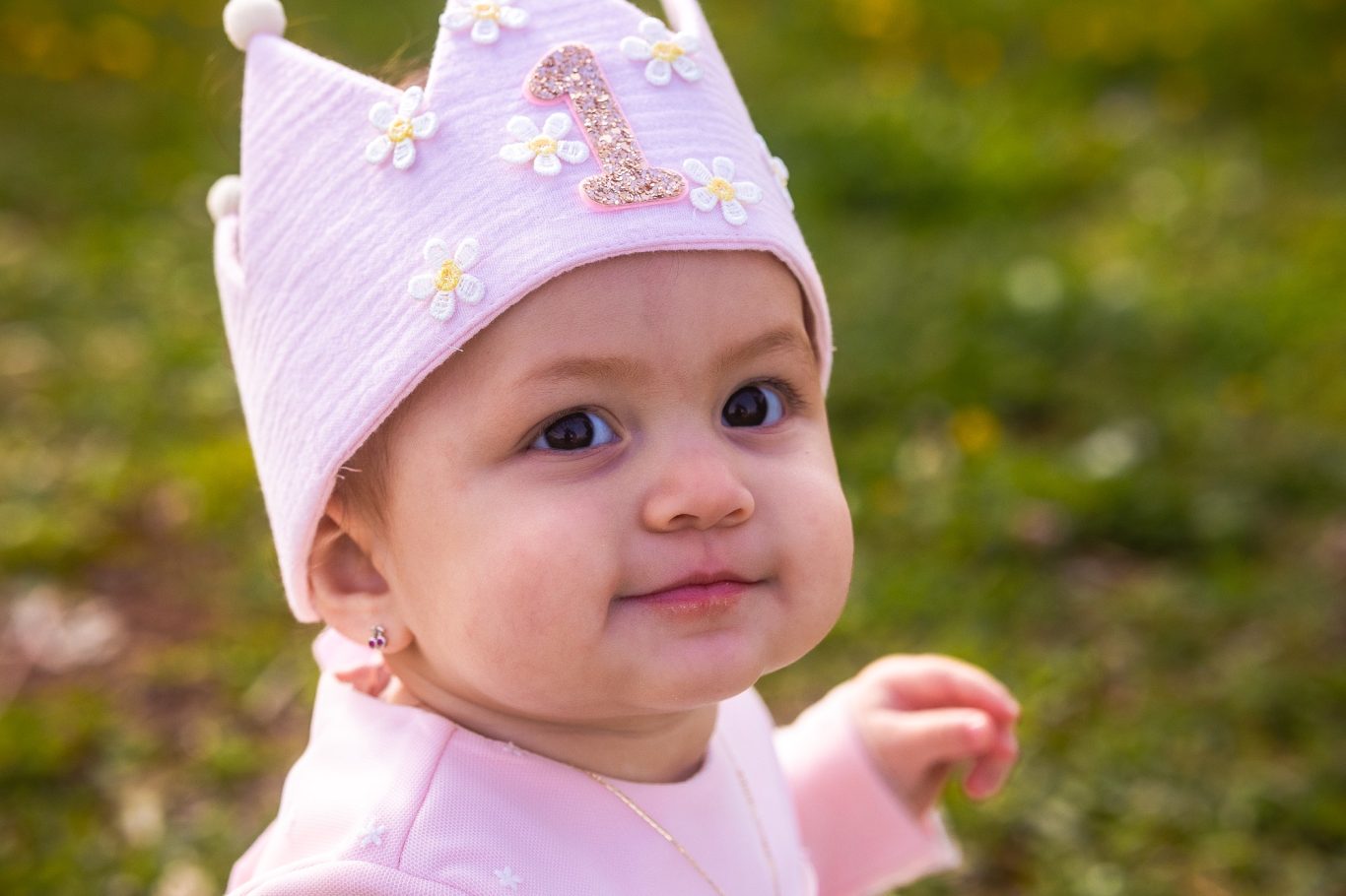 Bebé sonriente con un gorro de cumpleaños decorado, de pie en un entorno natural.