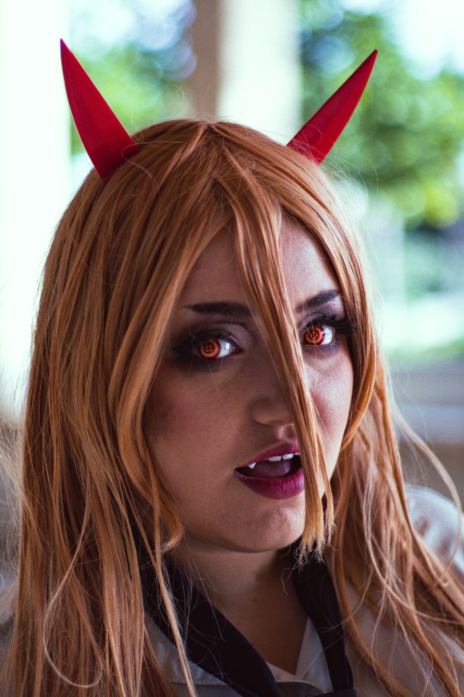 Mujer con cabello rubio y cuernos rojos, mirada intensa y labios oscuros.