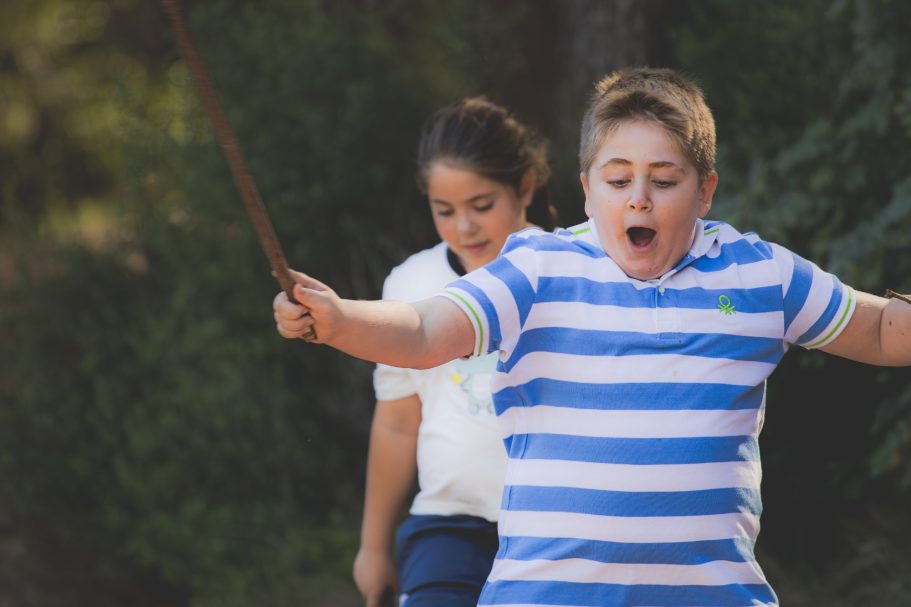 Niño emocionado saltando la cuerda con una niña detrás en un entorno natural.