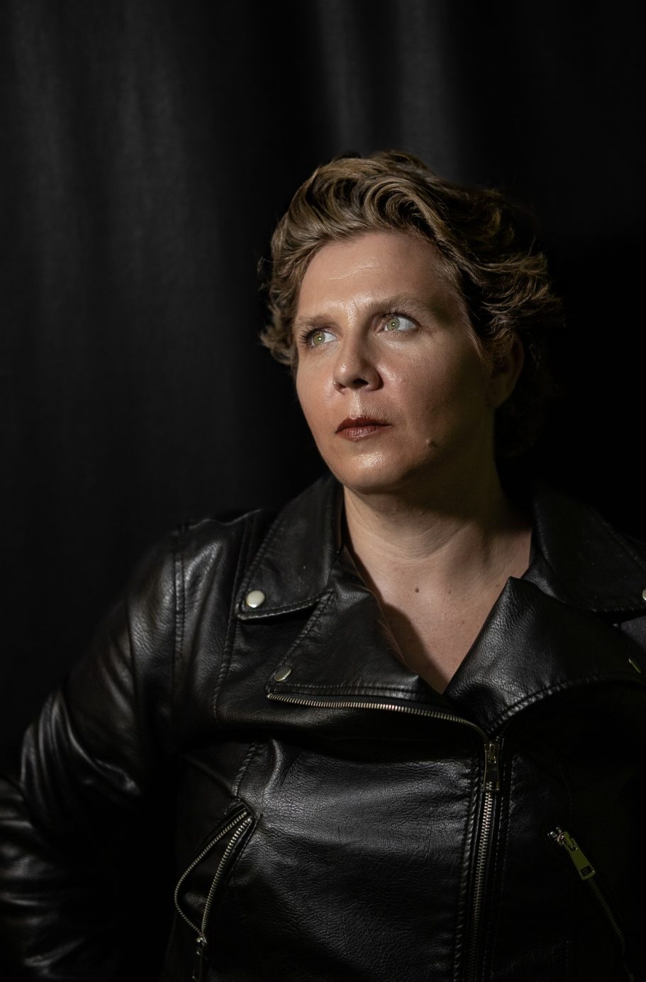 Mujer con chaqueta de cuero, mirada pensativa, fondo oscuro.