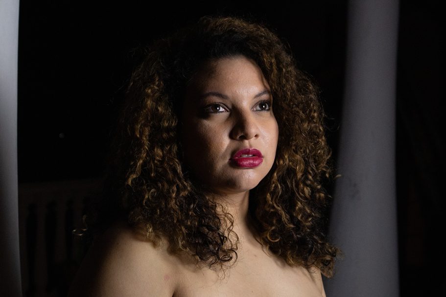 Mujer con cabello rizado y oscuro, mirando hacia arriba con labios pintados de rojo.