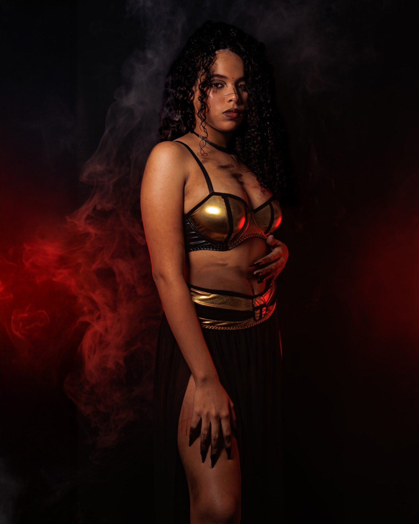 Mujer con cabello rizado, vistiendo un top dorado y falda negra, rodeada de humo y luces.