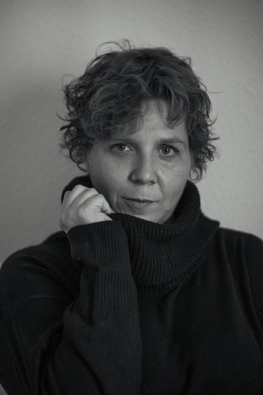 Mujer con cabello rizado y suelto, vistiendo un suéter oscuro, mirando a la cámara.