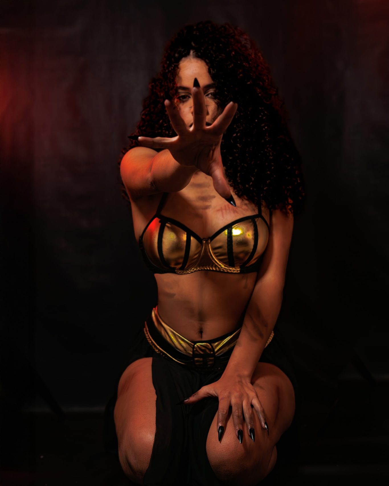 Mujer con traje dorado y oscuro, sentada, con la mano extendida hacia adelante.