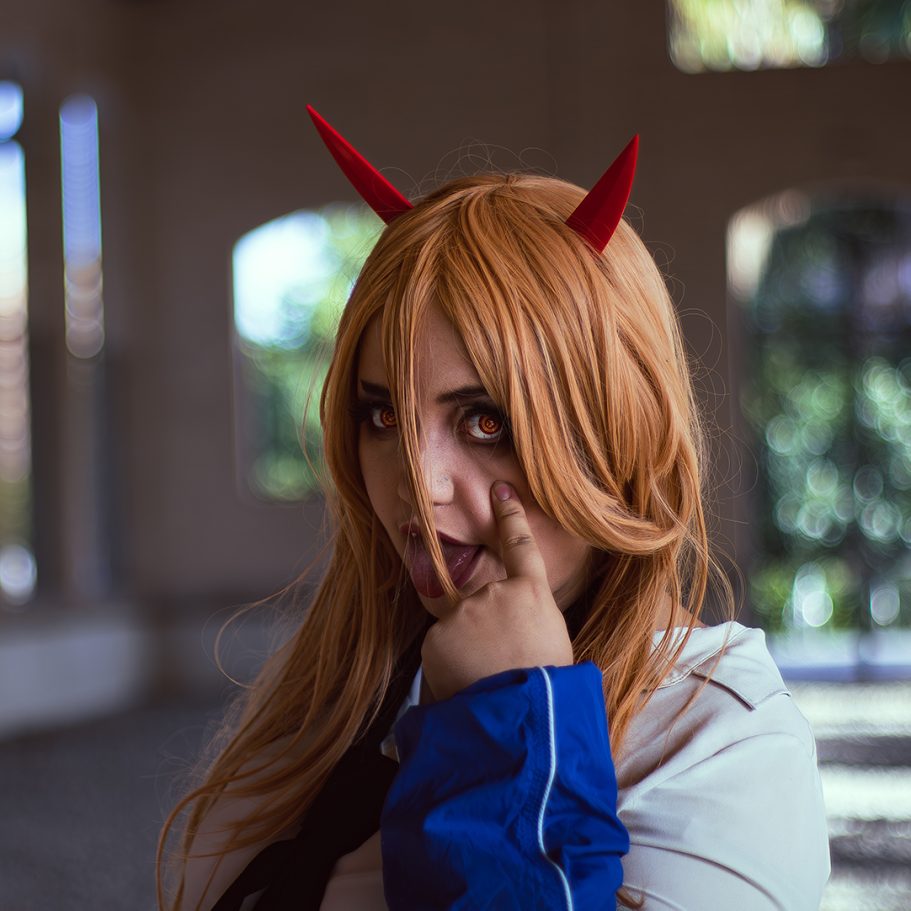 Mujer con cabello largo y orejas de demonio, vistiendo una chaqueta azul y haciendo un gesto.