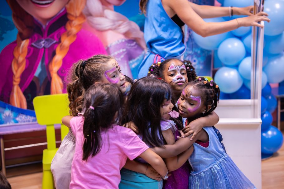Niñas sonriendo y abrazándose en un ambiente festivo con decoraciones coloridas.