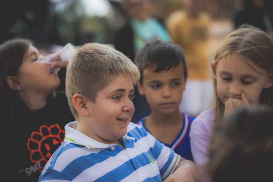 Niño sonriente con pelo corto, rodeado de otros niños en un ambiente alegre.