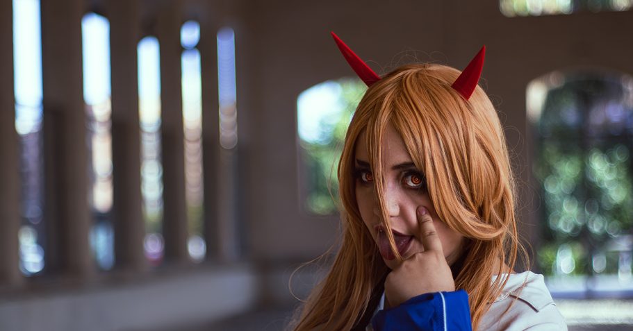 Chica con peluca larga y cuernos rojos, posando con expresión juguetona en un entorno urbano.