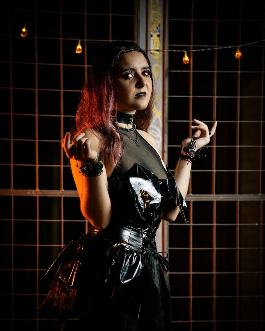 Joven con cabello oscuro y rojizo, vestida de manera gótica, en un entorno con luces tenues.