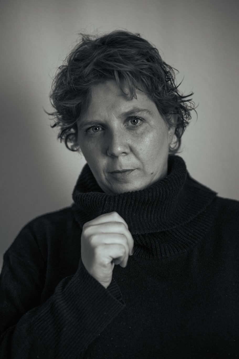 Mujer con cabello corto y rizado, vistiendo un suéter oscuro, mirando hacia la cámara.