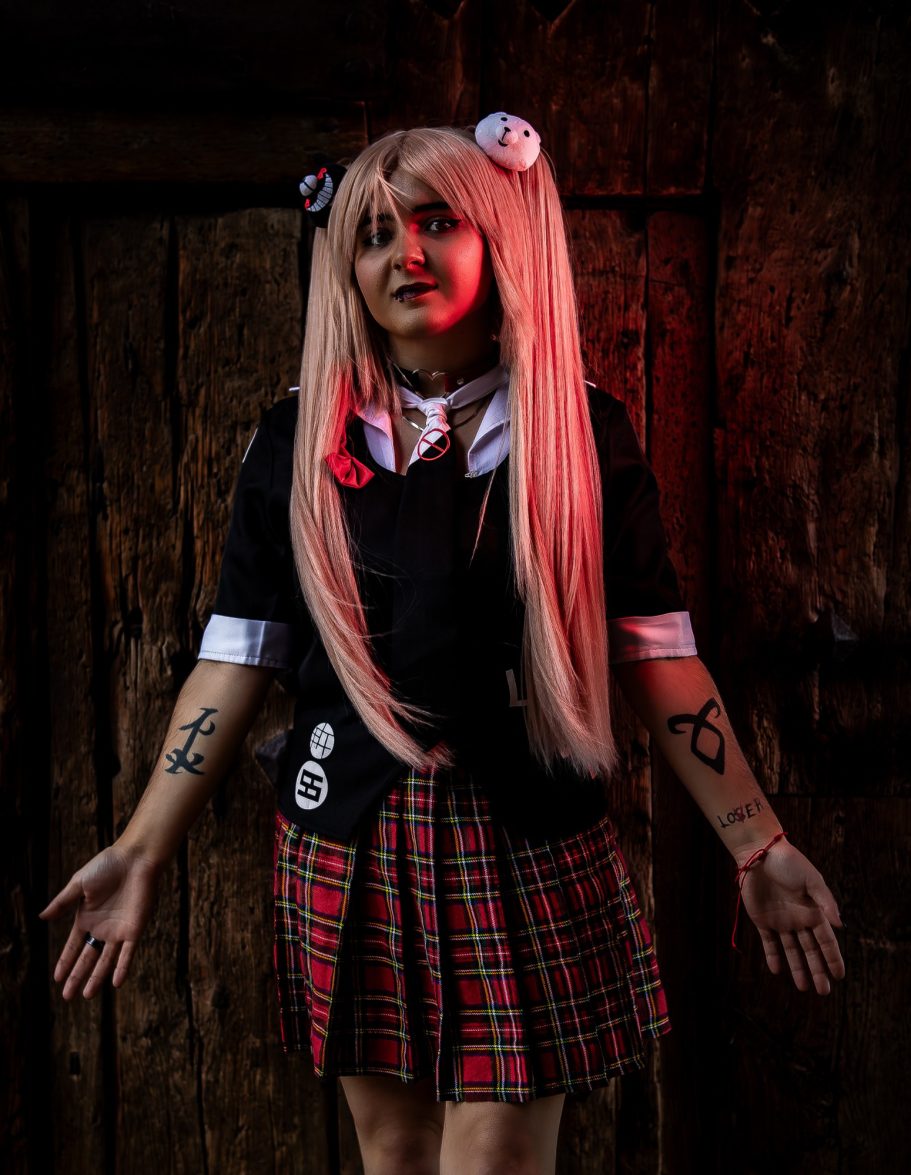 Persona con cabello largo y rubio, vistiendo uniforme escolar con una falda de cuadros.